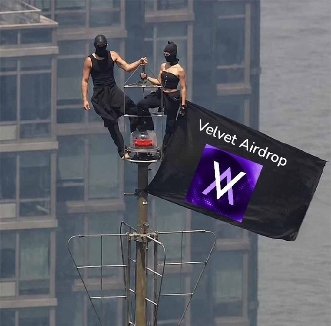 Two masked individuals in black outfits sit atop a structure holding a black flag that reads 'Velvet Airdrop' with a purple 'VV' logo, positioned against a city backdrop.