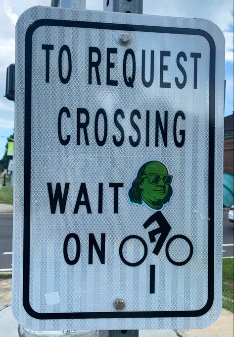 A street sign reads "TO REQUEST CROSSING WAIT ON" with a cyclist icon that has been humorously modified with a green Pepe the Frog face wearing sunglasses, and a peace sign hand. The meme plays on "$bread is baking" by depicting Pepe waiting patiently for crossing permission—likely a tongue-in-cheek nod to "waiting for the bread" in crypto slang.