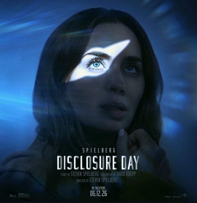 The image features a woman with long brown hair, looking at the camera while wearing a tan jacket. She has blue eyes that are the main focus of the picture. The background appears to be a dark blue color, which contrasts with her light-colored hair. There is no text in the image, and it does not contain any other objects or people.