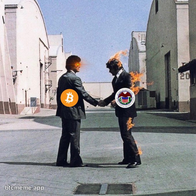 A photoshopped meme showing two men in suits shaking hands with Bitcoin and U.S. government department logos over their faces, with flames edited around them, watermarked 'btcmeme.app'.