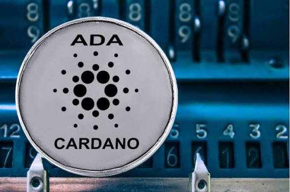 A close-up of an ADA Cardano cryptocurrency coin resting on the keys of a blue typewriter.