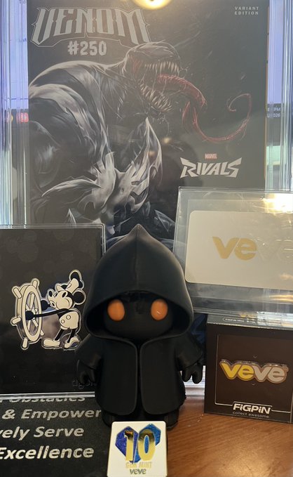 A display featuring a Venom #250 Variant Edition comic book, a black-hooded vinyl figure with orange eyes, and VeVe branding with a '10 Years' badge.