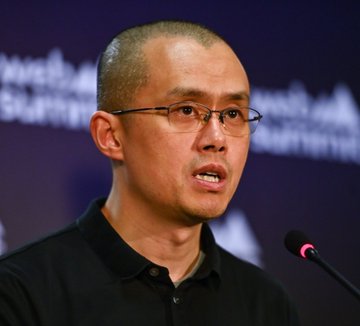 The image features a man wearing glasses, standing behind a microphone with his mouth open as if he's speaking or giving a speech. The background of the image shows a blue wall with white text that reads "BREAKING NEWS: #Binance CZ; he said he believes more than ever that crypto won' t disappear and that it will grow in a much bigger way." This suggests that the man is addressing an important topic related to cryptocurrency, possibly discussing its future growth or the impact of Bitcoin on the financial world.