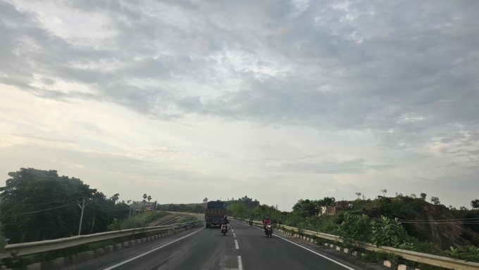 A view from a vehicle driving on a highway under a cloudy sky, with motorcycles and a truck visible on the road ahead.