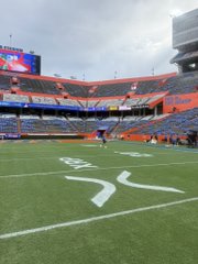 An empty football stadium with a green field marked with yard lines and a large screen visible in the stands.