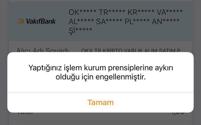 A screenshot from the VakifBank mobile app shows a popup message reading "Yaptığınız işlem kurum prensiplerine aykırı olduğu için engellenmiştir." (Your transaction has been blocked because it is against the institution's principles) over a background displaying the OKX TR crypto asset buying/selling page. The user is tagging VakifBank and OKX Turkey support, apparently frustrated that the bank blocked their cryptocurrency transaction.