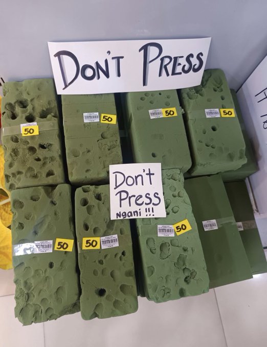 A stack of green floral foam blocks in packaging marked '50', labeled with handwritten signs reading 'Don't Press' and 'Don't Press Ngani !!!'.