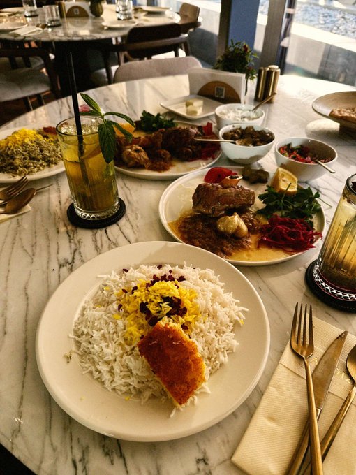 A table spread of food at a restaurant featuring a plate of saffron rice with grilled salmon, grilled meats with vegetables, and various side dishes.