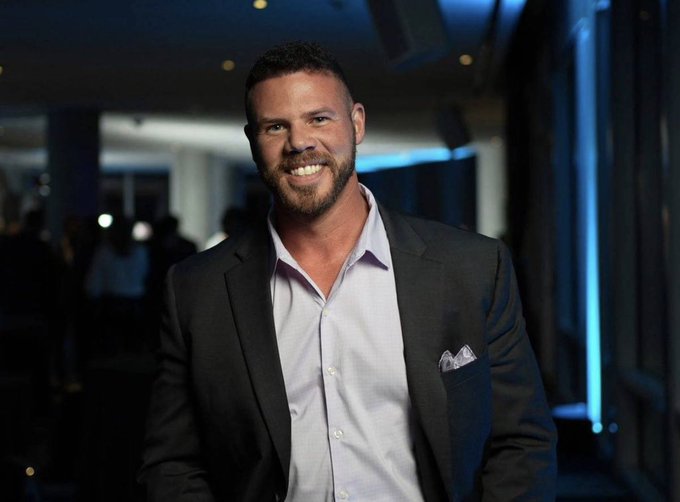 Jake Claver, pictured smiling in a dark blazer at what appears to be an evening event, is the subject of the post discussing his bullish prediction that XRP could reach $1,500+ by 2026, as stated on the CryptoDYL News podcast.
