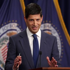 Former Federal Reserve Vice Chair Kevin Warsh, who is expected to deliver remarks at the Jackson Hole symposium, is shown speaking at a podium with the U.S. Department of Justice seal in the background—relevant as investors weigh his tone on monetary policy amid a Bank of America survey showing 53% expect neutral, 31% hawkish, and only 7% dovish commentary.