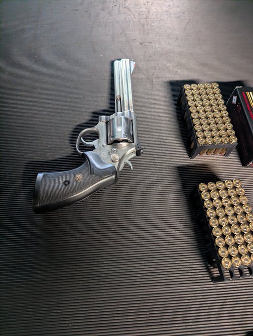 A large silver revolver with a long barrel lying next to boxes of ammunition on a black ribbed surface.