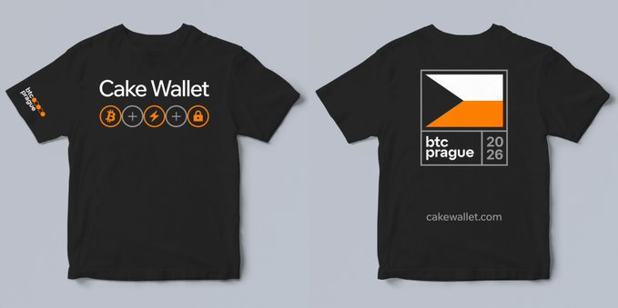 The image features a black t-shirt laid out flat against a gray background with the text "Cake Wallet" written on it. The t-shirt has an orange and white design on the front, which includes a square with the Czech flag symbolizing the event taking place at the Bitcoin Prague conference in Prague, Czech Republic.