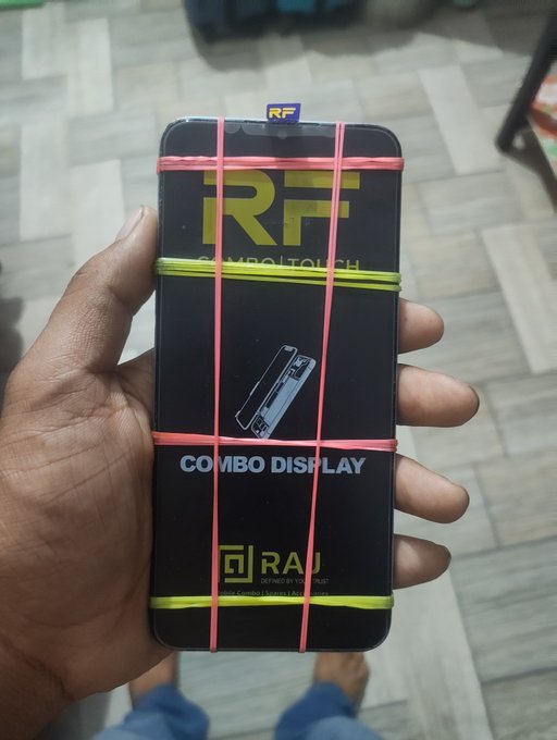 A hand holding a new smartphone in its packaging, secured with decorative pink and yellow rubber bands, displaying the "RF Symbol Touch" branding and "COMBO DISPLAY."