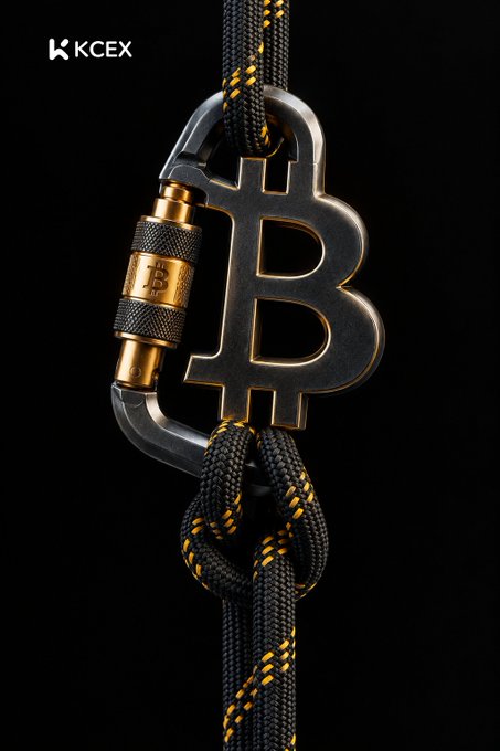 A KCEX promotional image featuring a metallic Bitcoin logo secured by a carabiner and threaded through a black and yellow braided rope against a dark background.