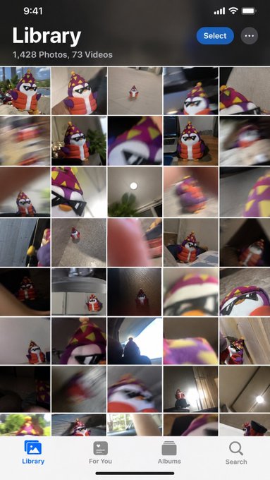 iOS Photos app Library view showing 1,428 photos and 73 videos, predominantly featuring a plush toy in a purple, orange, and yellow costume, with many images being blurry.