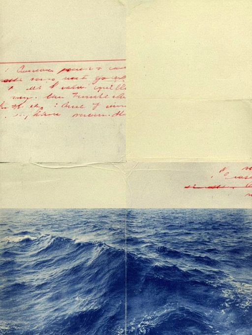 An artistic photograph showing a piece of folded paper with red handwritten text positioned above an image of ocean waves, creating a layered visual effect.