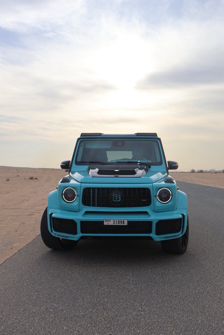A turquoise Mercedes-Benz G-Wagon with a Dubai license plate reading "31086" sits on a desert road, embodying luxury and status. The caption "GM (get money)" complements the image, as the G-Wagon is a symbol of wealth and success.