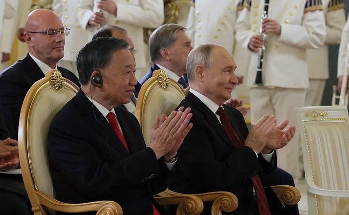 Chinese President Xi Jinping and Russian President Vladimir Putin sit side-by-side in ornate gold chairs, both wearing earpieces and clapping during a formal ceremony.