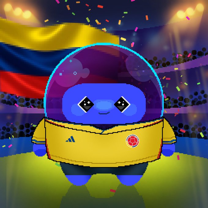 A cute blue alien mascot wearing a yellow Colombia national football jersey stands on a stadium field with a Colombian flag and confetti in the background, representing Dlicom's World Cup Collection #19 featuring Colombia.