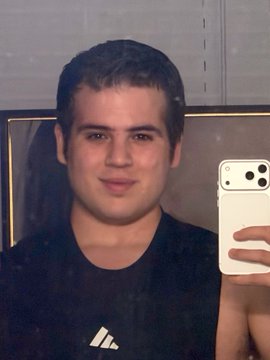 A mirror selfie of a young man wearing a black Adidas shirt, holding a white iPhone with the camera visible.