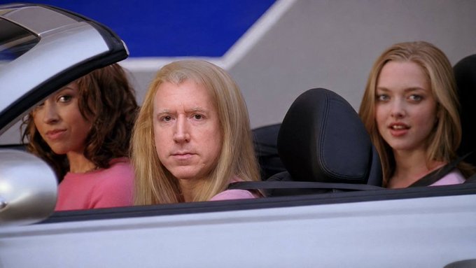 Adam Sandler in "The Waterboy" stares out of a convertible alongside two fellow actors, which humorously matches the financial aim hinted at in the accompanying post.  His roughly two and a half-decade-old haircut looks foolishly formal given the scary pink crushing the women.