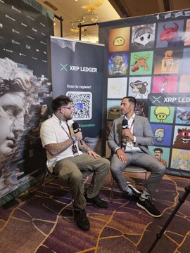Two men sit on stools at an XRP Ledger booth during the RareEvo event in Las Vegas, with a backdrop featuring a grid of colorful NFT artwork and the "XRP LEDGER" logo alongside a scannable QR code. The setup directly reflects the post's highlight of showcasing the XRP Ledger ecosystem, infrastructure, and creators to attendees.