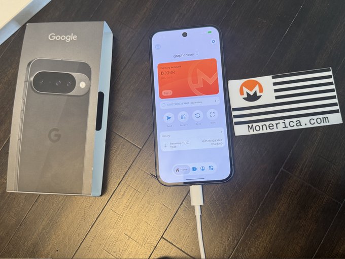 A photograph showing a Google Pixel smartphone box next to the phone displaying a Monerica.com screen (grapheones app) with XMR balance, and a Monerica.com card on a wooden surface.