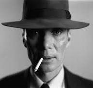 A black and white portrait of a man wearing a dark fedora and suit, with a cigarette dangling from his mouth, resembling an old-fashioned detective.