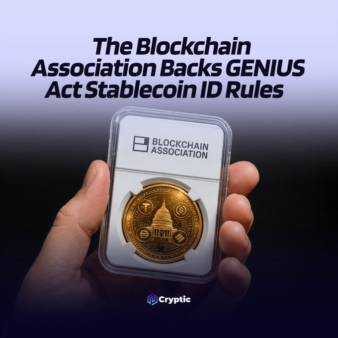 A hand holds a graded gold coin encased in a "Blockchain Association" slab, beneath the headline "The Blockchain Association Backs GENIUS Act Stablecoin ID Rules" and a "Cryptic" logo. The image visually reinforces the article's message by combining the association's branding with a symbolic gold coin representing stablecoins, illustrating the group's endorsement of the proposed identification framework.