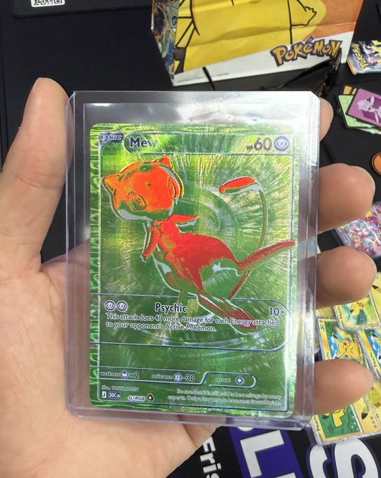 A hand holds a holographic custom Pokémon card featuring 'Mew' with artwork of an orange and red creature.
