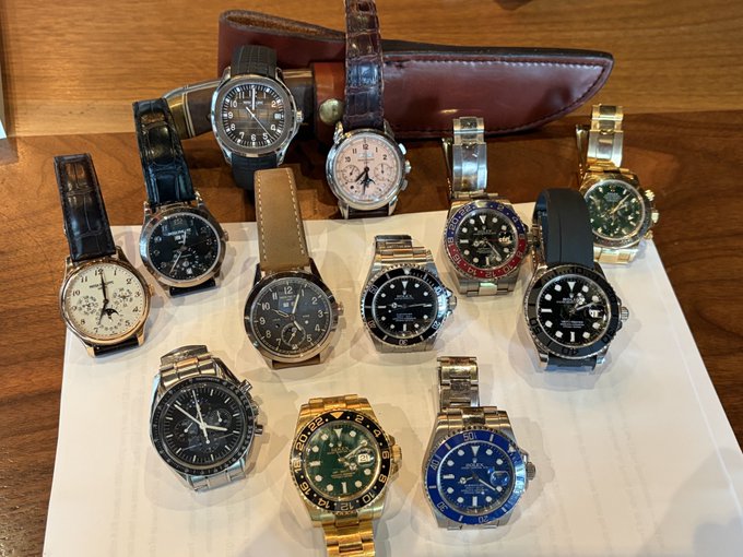 A collection of around a dozen luxury watches, including several Rolex models with GMT and Submariner bezels, IWC, Jaeger-LeCoultre, and chronograph pieces, arranged on a white surface in front of a leather watch case, showcasing the owner's "favorite" timepieces as part of their watch collection ("Watch degens").