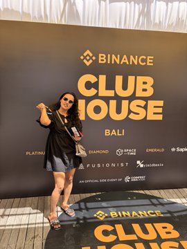 A woman poses in front of a Binance Clubhouse Bali backdrop featuring logos for Platinum, Diamond, Space Travelers, Emerald, Fusionist, and Super Indonesia as sponsors.