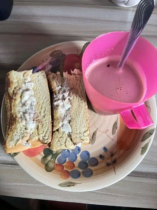 A meal consisting of a tuna sandwich cut in half and a pink mug filled with what appears to be coffee or tea with milk.