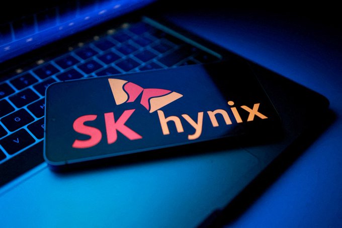 A smartphone displaying the "SK hynix" logo rests on a laptop keyboard, illuminated by blue lighting. The image visually reinforces the article about SK Hynix's potential partnership with Intel to manufacture memory products in the United States.