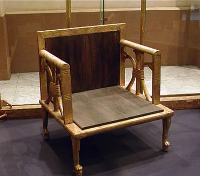 An ancient Egyptian gilded chair with lion-paw feet and bound-reed decorative motifs displayed in a museum case.