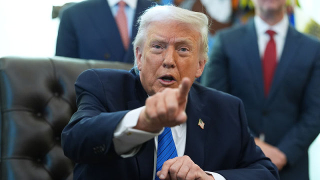 Former President Donald Trump, with his signature blonde hair and a stern expression, gestures emphatically while seated in a tufted leather chair, dressed in a dark suit with a blue tie and American flag pin, as officials stand behind him in what appears to be the White House, setting the stage for his meeting with cryptocurrency industry leaders.