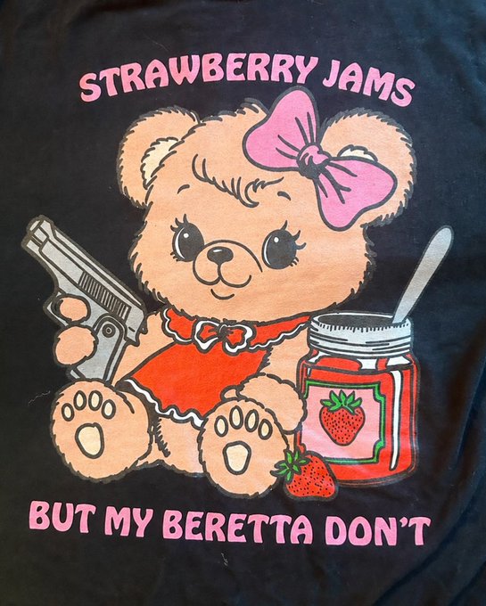 A black t-shirt featuring a vintage cartoon bear with a pink bow holding a gun and a jar of strawberry jam, with pink text reading "STRAWBERRY JAMS" and "BUT MY BERETTA DON'T".
