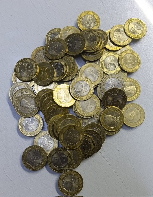 A pile of gold and silver coins, appearing to be South African rand coins with '5' denominations visible, scattered on a white surface.