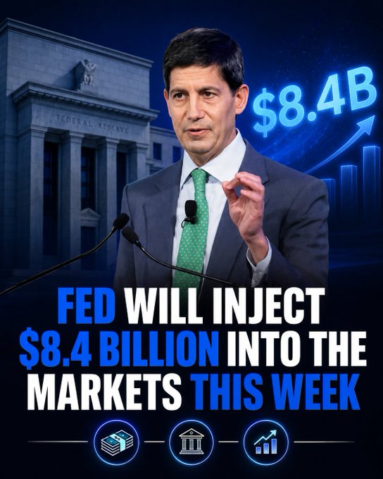 A man in a suit speaking at a podium with the Federal Reserve building in the background, with text announcing 'FED WILL INJECT $8.4 BILLION INTO THE MARKETS THIS WEEK' and a '$8.4B' graphic with an upward arrow.
