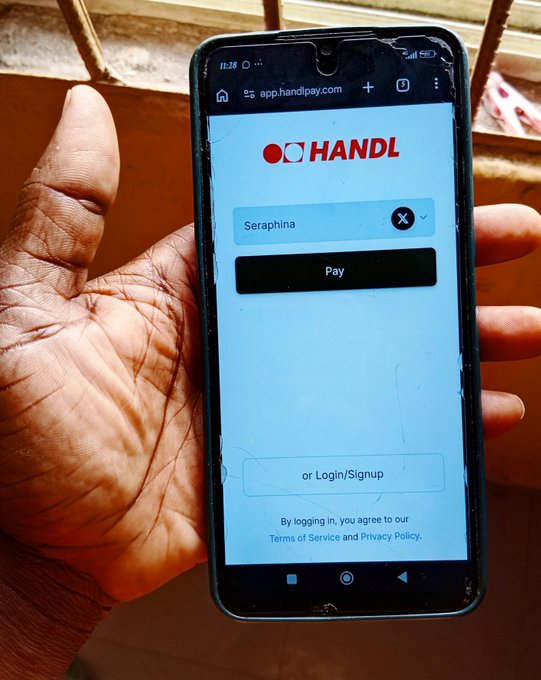 A hand holding a cracked smartphone displaying the HANDL payment app at 'app.handlpay.com', with a field showing 'Seraphina' and buttons for 'Pay' and 'or Login/Signup'.