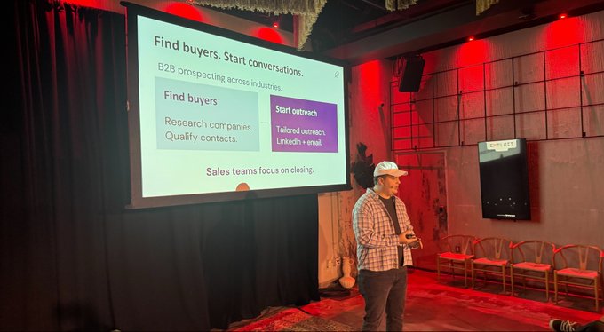 A man giving a business presentation on stage about 'Find buyers' and 'Start outreach' in B2B prospecting.