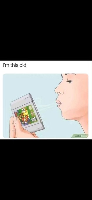 A wikiHow-style illustration captioned 'I'm this old' depicting a person blowing into a Nintendo 64 game cartridge.