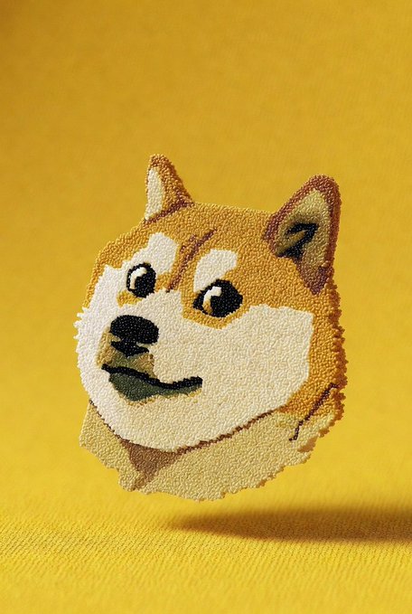 A tufted, rug-like sculpture of the iconic Shiba Inu dog—commonly associated with the Dogecoin cryptocurrency—floats against a bright yellow background. The textured artwork captures the breed's alert expression and reddish-tan coat, serving as a playful visual nod to the meme-inspired digital currency.