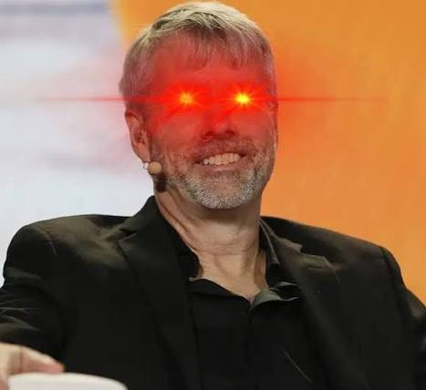 A man with gray hair and beard smiles while wearing a headset microphone, with red laser beams digitally added over his eyes giving a sci-fi effect.