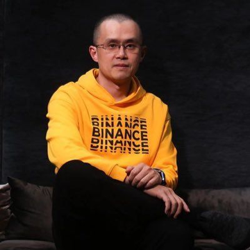 A man wearing a yellow "BINANCE" hoodie sits with crossed legs on a dark couch, appearing contemplative. The image is associated with CZ (@cz_binance), Binance's founder, who is reportedly planning to donate his remaining BNB and 币安人生 tokens from a Trust Wallet testing address to Giggle Academy before retiring the wallet as a burn address.
