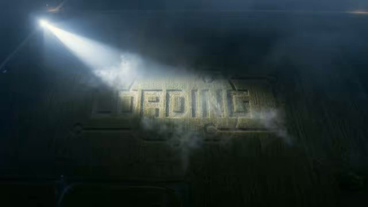 The image features a large, illuminated sign that reads "LOADING" with a spotlight shining on it. The background of the image shows a dark room or warehouse-like setting, which contrasts with the bright light from the spotlight. There are no other objects in the scene besides the sign and the spotlight.
