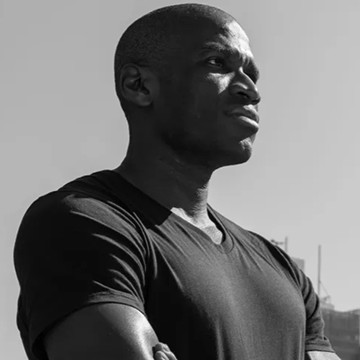 The image features a man with short hair wearing a black shirt against a white background. The photo appears to be in black and white, giving it a timeless quality. There are no texts or other objects present in the image. The main focus is on the man's facial expression as he looks off into the distance.