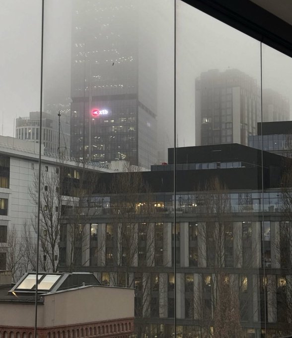 A misty, rainy cityscape view through a window of high-rise office buildings, including one with an XIB bank sign.