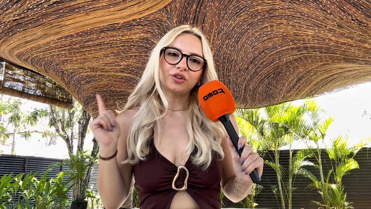 A blonde woman wearing glasses holds an orange "FOMO" branded microphone while gesturing under a woven canopy, seemingly reporting on the upcoming Solana event in Singapore.