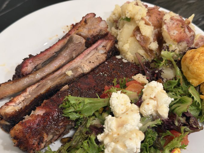 A plate of smoked ribs, potato salad, and a fresh salad with crumbled cheese and ranch dressing is served, with a deviled egg peeking out on the side—matching the "lil egg action" mentioned in the post.